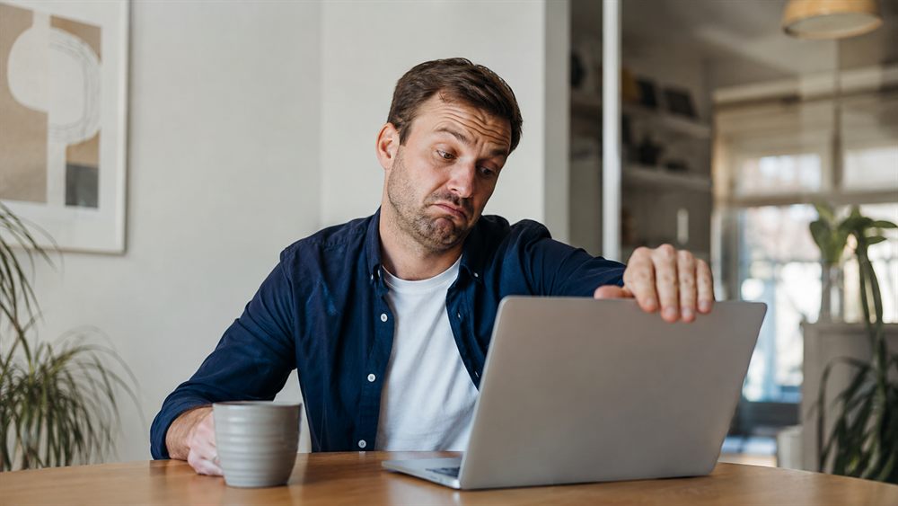 En skeptisk mand kigger tvivlende på sin bærbare og er klar til at lukke låget