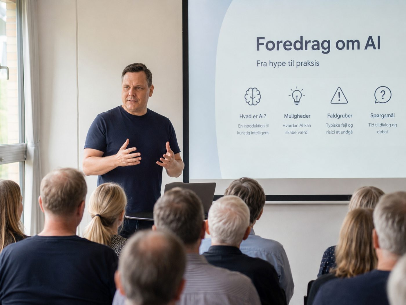 Mickey holder foredrag om AI foran en engageret forsamling med en præsentation, der siger “Foredrag om AI – fra hype til praksis”